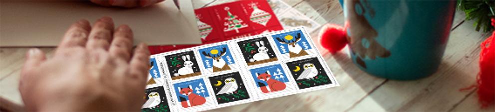 A person addressing a letter with 一流的邮件 Forever® holiday stamps on the table.
